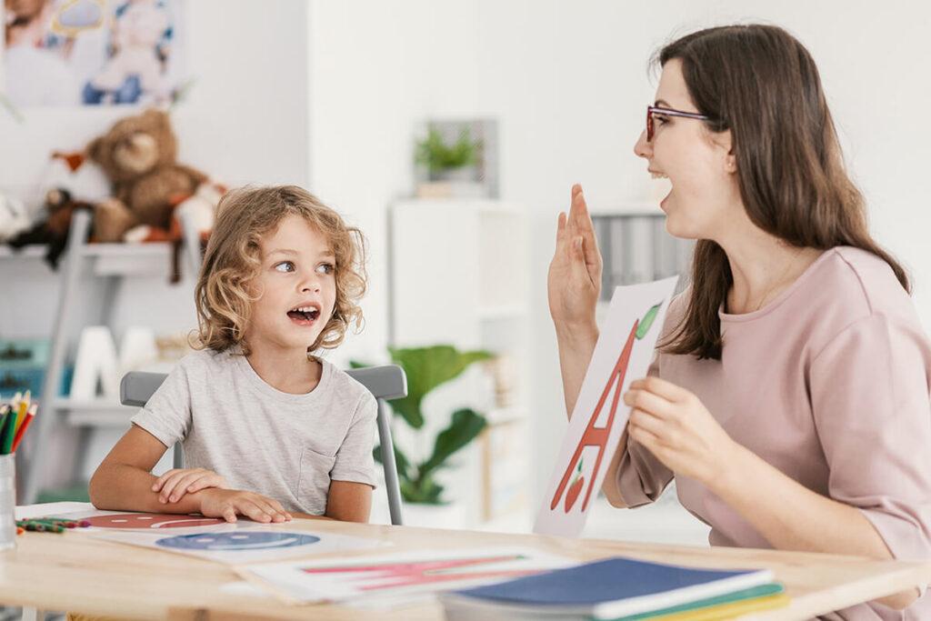A young child sitting with an adult holding a sign with the letter "A"