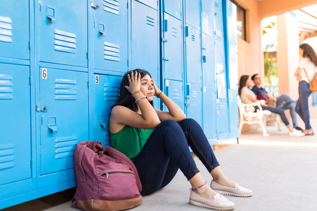 Young latin girl leaning on blue lockers stressed